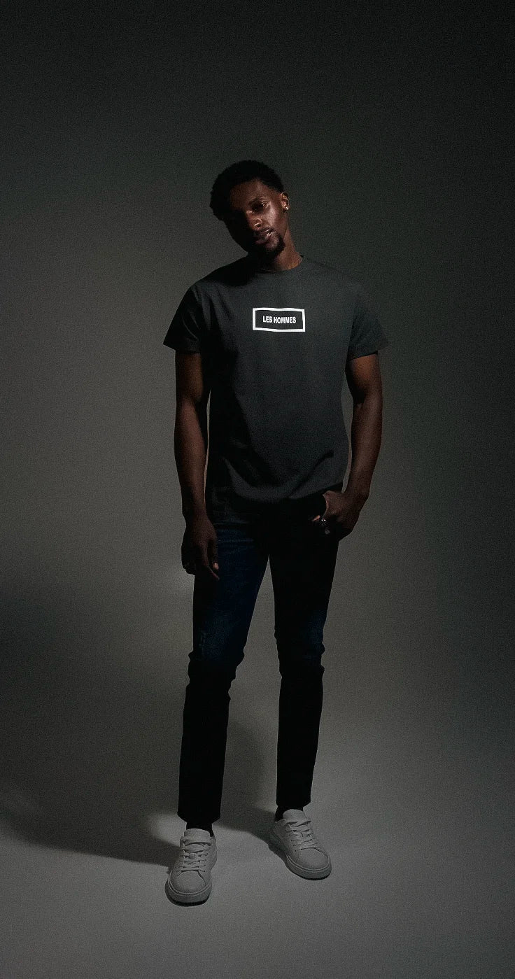 Person wearing a dark t-shirt with a Les Hommes logo on a gray background
