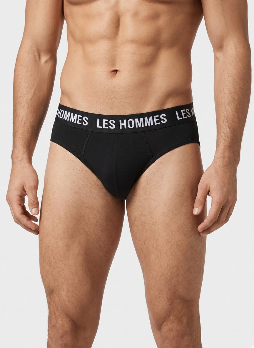 man wearing black briefs with a wide elastic waistband reading Les Hommes