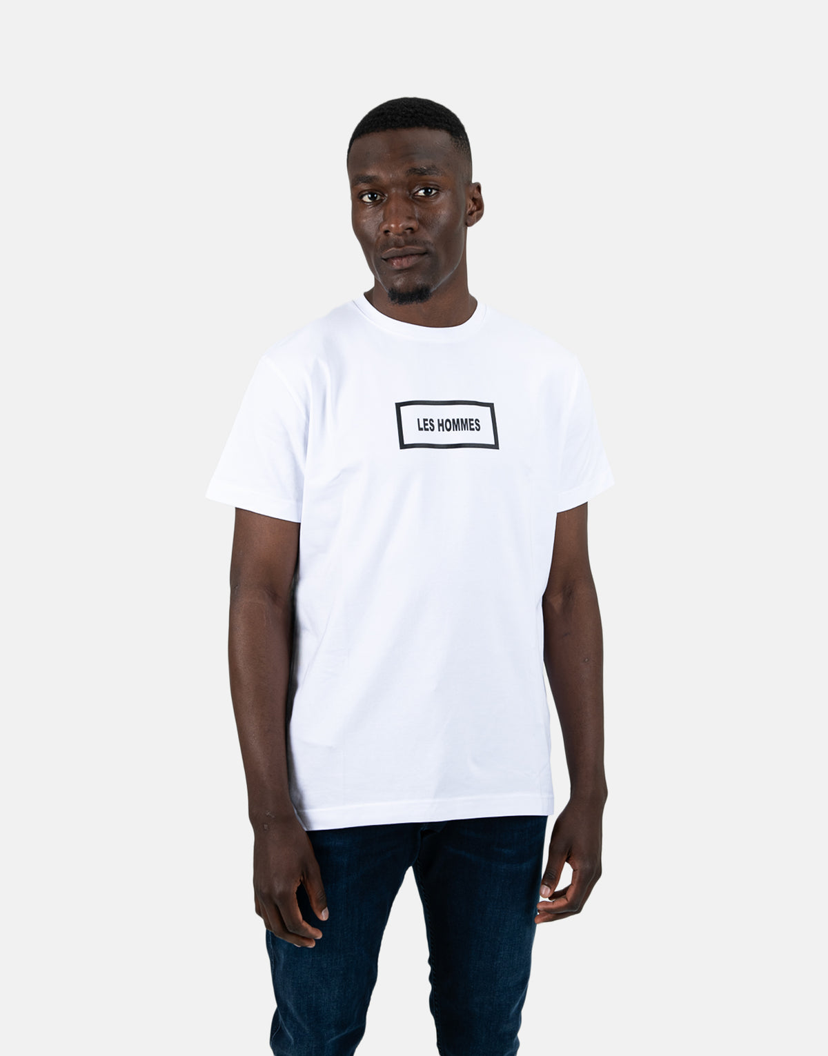 man wearing white short sleeve t-shirt with a black outlined rectangle logo reading Les Hommes