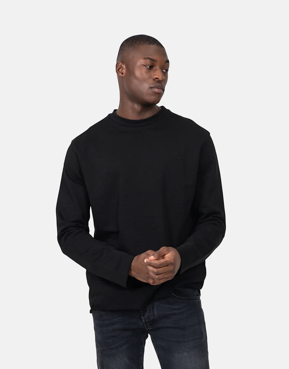 A male model wears a black Les Hommes Dragonfly crew-neck long-sleeve sweatshirt with dark jeans, posed against a white