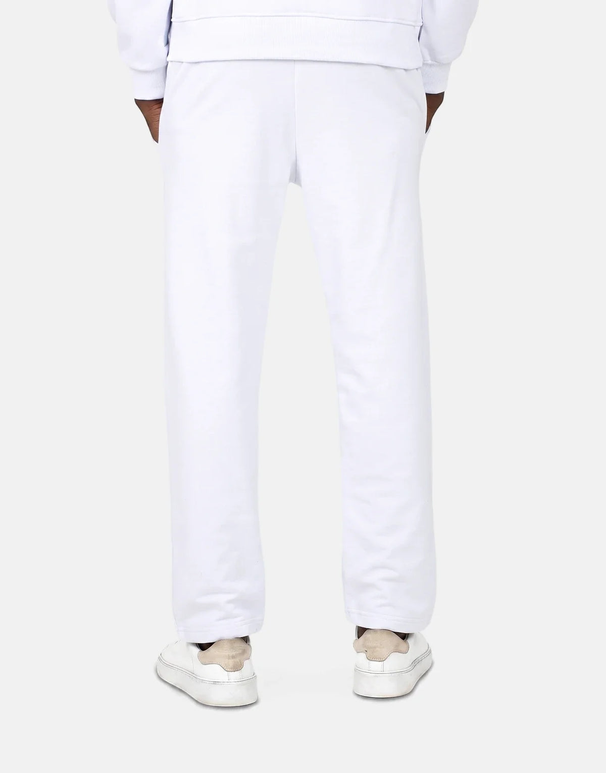 Men's Les Hommes white jogger sweatpants shown from the back, paired with white sneakers. The model is standing with hands
