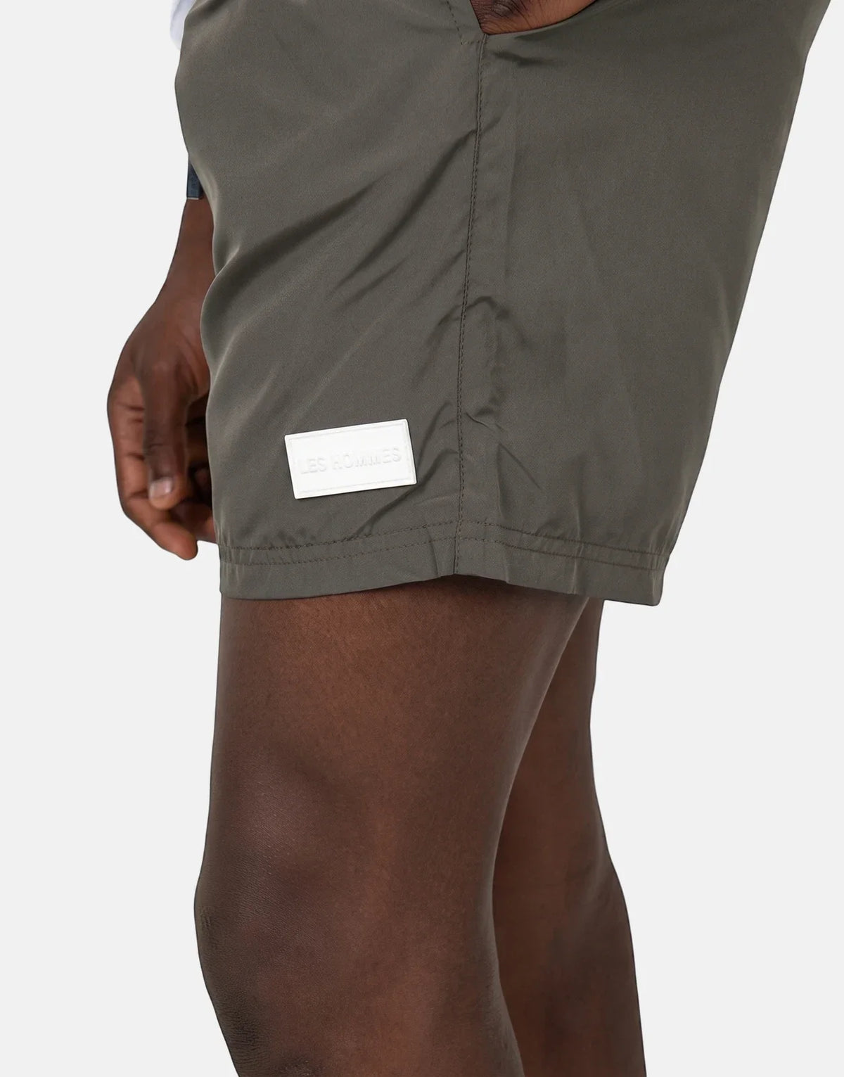Close-up of Les Hommes olive green swim shorts worn by a model, featuring a white rectangular logo patch on the thigh.