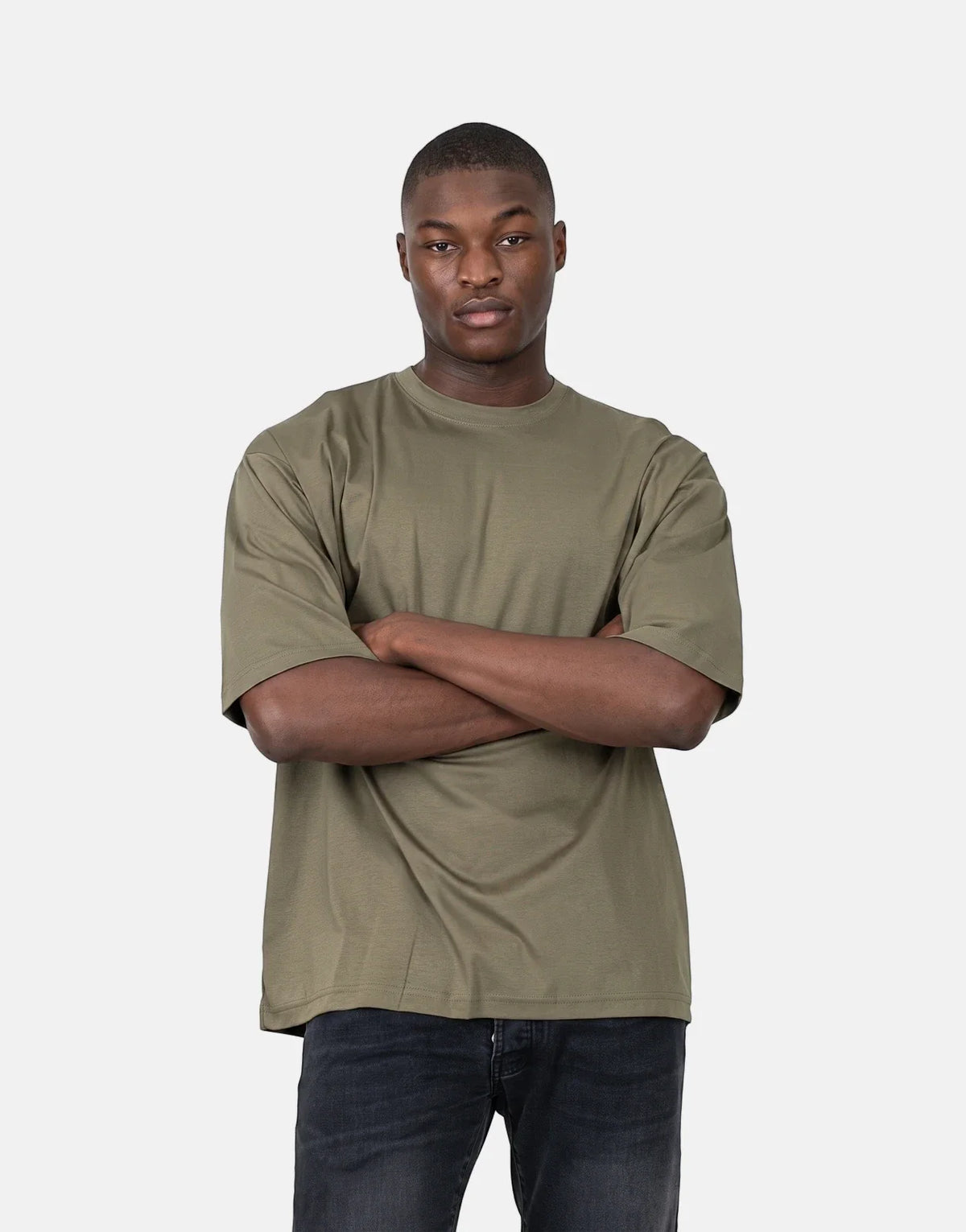 Young man wearing an olive green Les Hommes Over Logo Back T-Shirt and black jeans with arms crossed, photographed from the