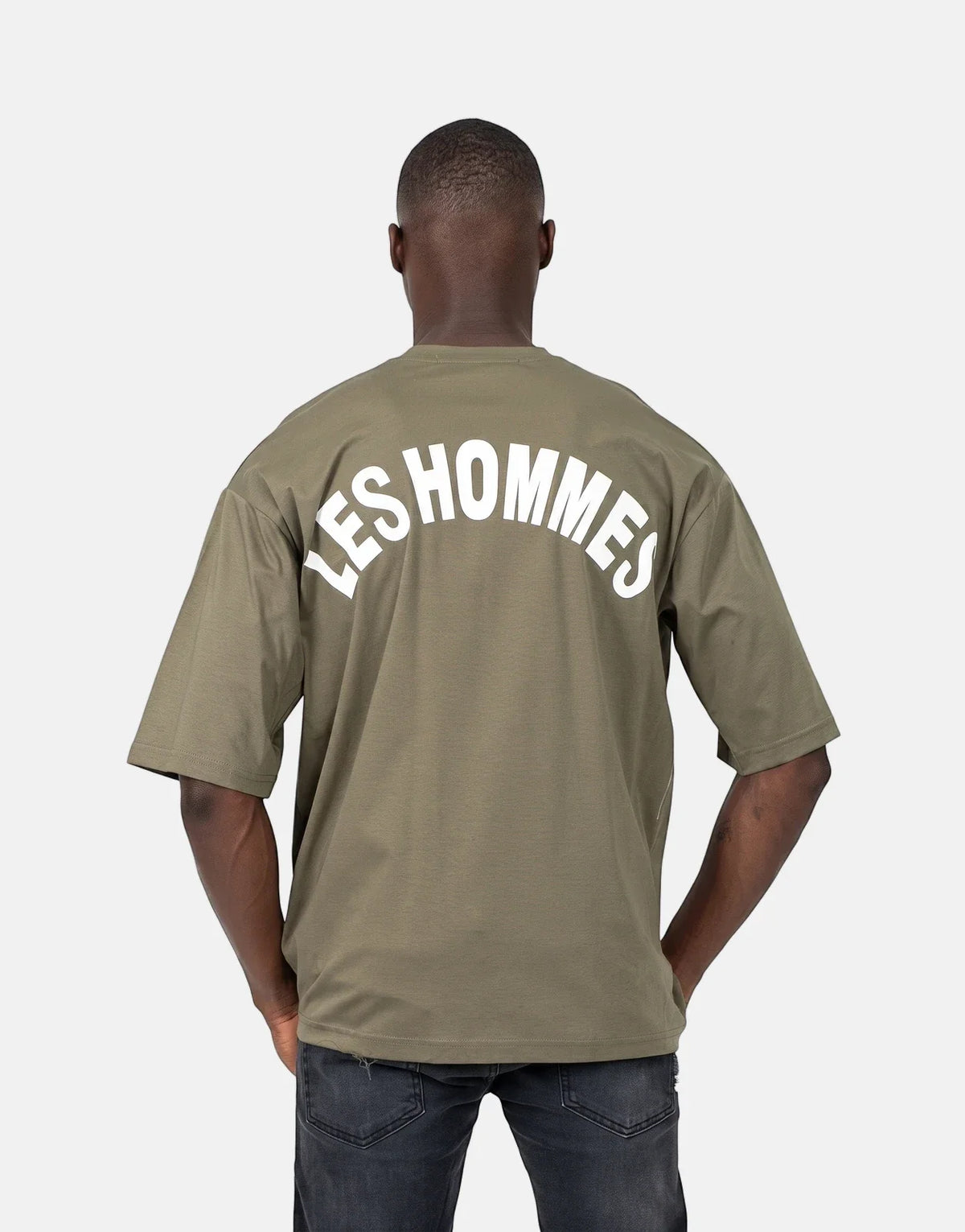 A male model wearing a green Les Hommes t-shirt with a white 'LES HOMMES' logo across the back, viewed from behind.