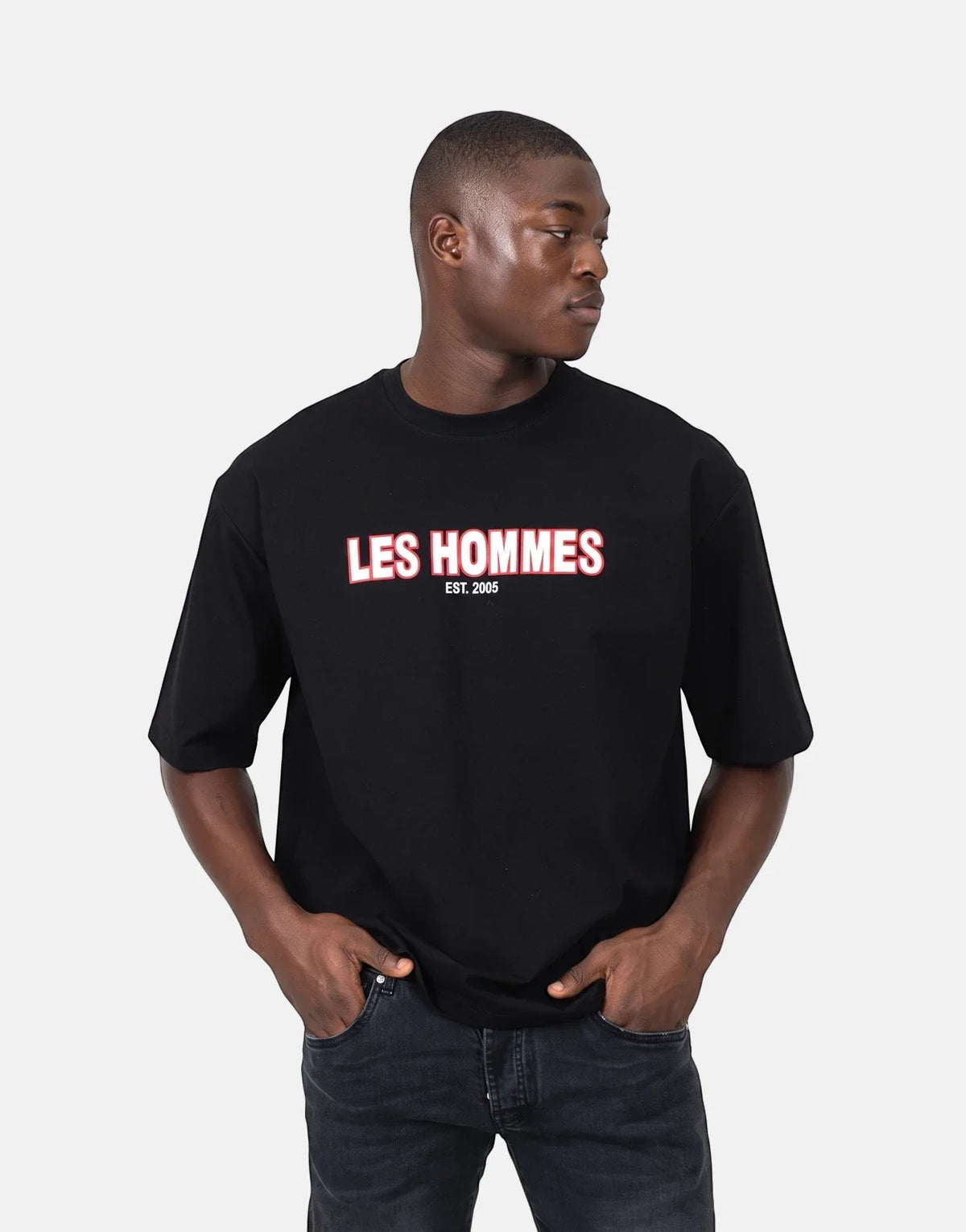 Male model wearing a black Les Hommes Over Rubber Print T-Shirt paired with dark wash jeans, front view.