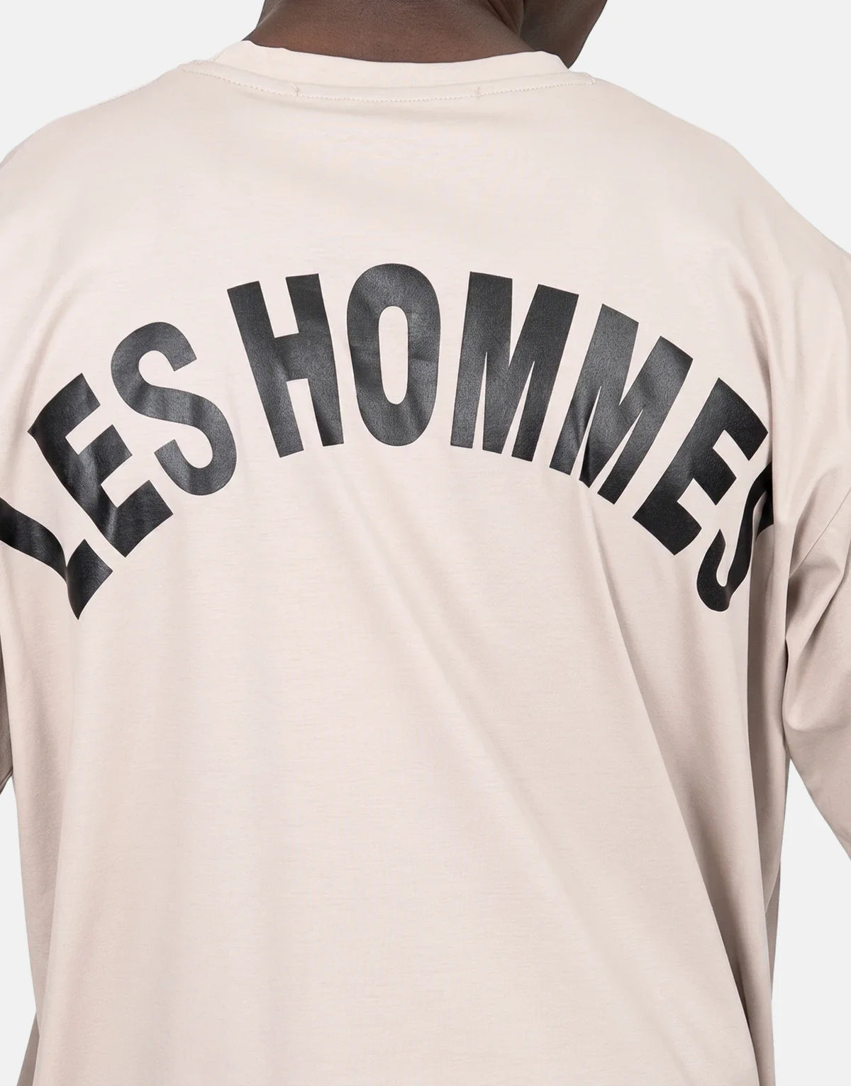 Back view of a Les Hommes oversized t-shirt in light beige, featuring a large arched black logo print on the back.