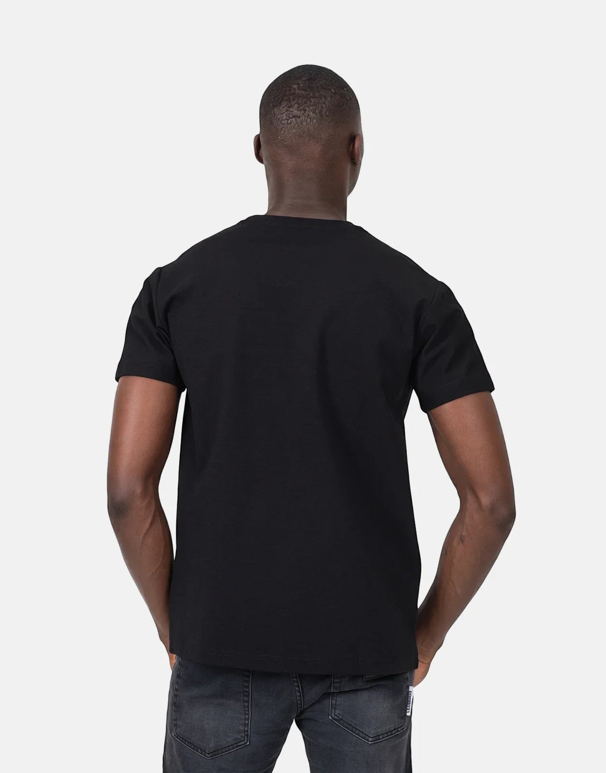 Back view of a Black man wearing a plain black Les Hommes t-shirt and dark grey jeans in a studio shot.