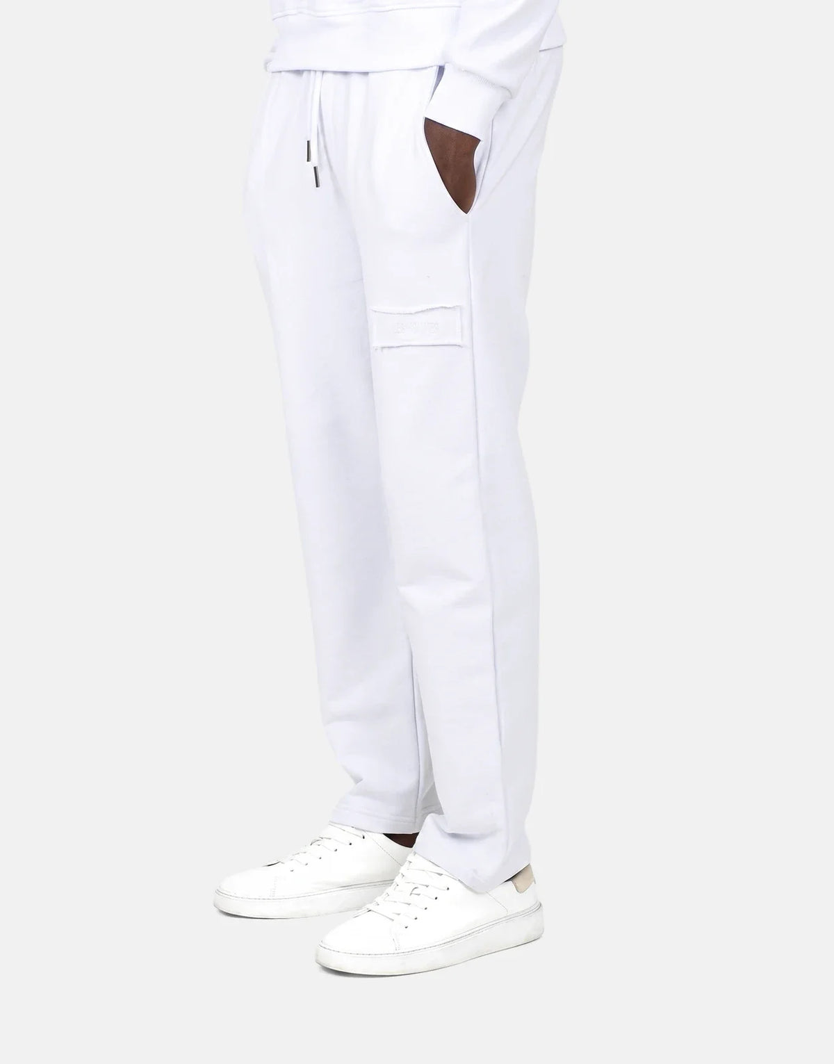Men's Les Hommes white jogger sweatpants and white sneakers in a profile view, featuring a distressed patch and drawstrings.