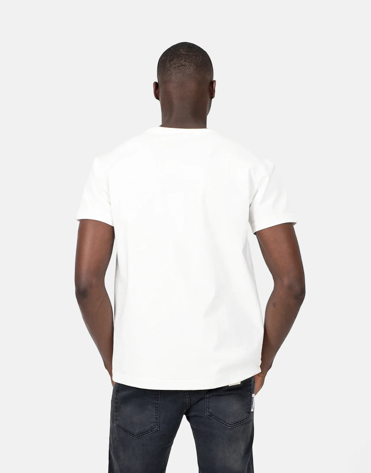 Back view of a man wearing a plain white short-sleeve crew neck t-shirt and dark wash jeans, standing casually.
